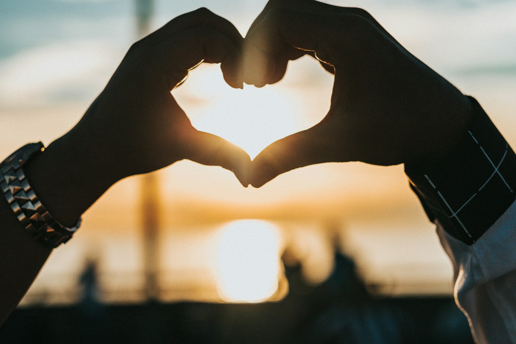 A couple forming a heart with their hands at sunset